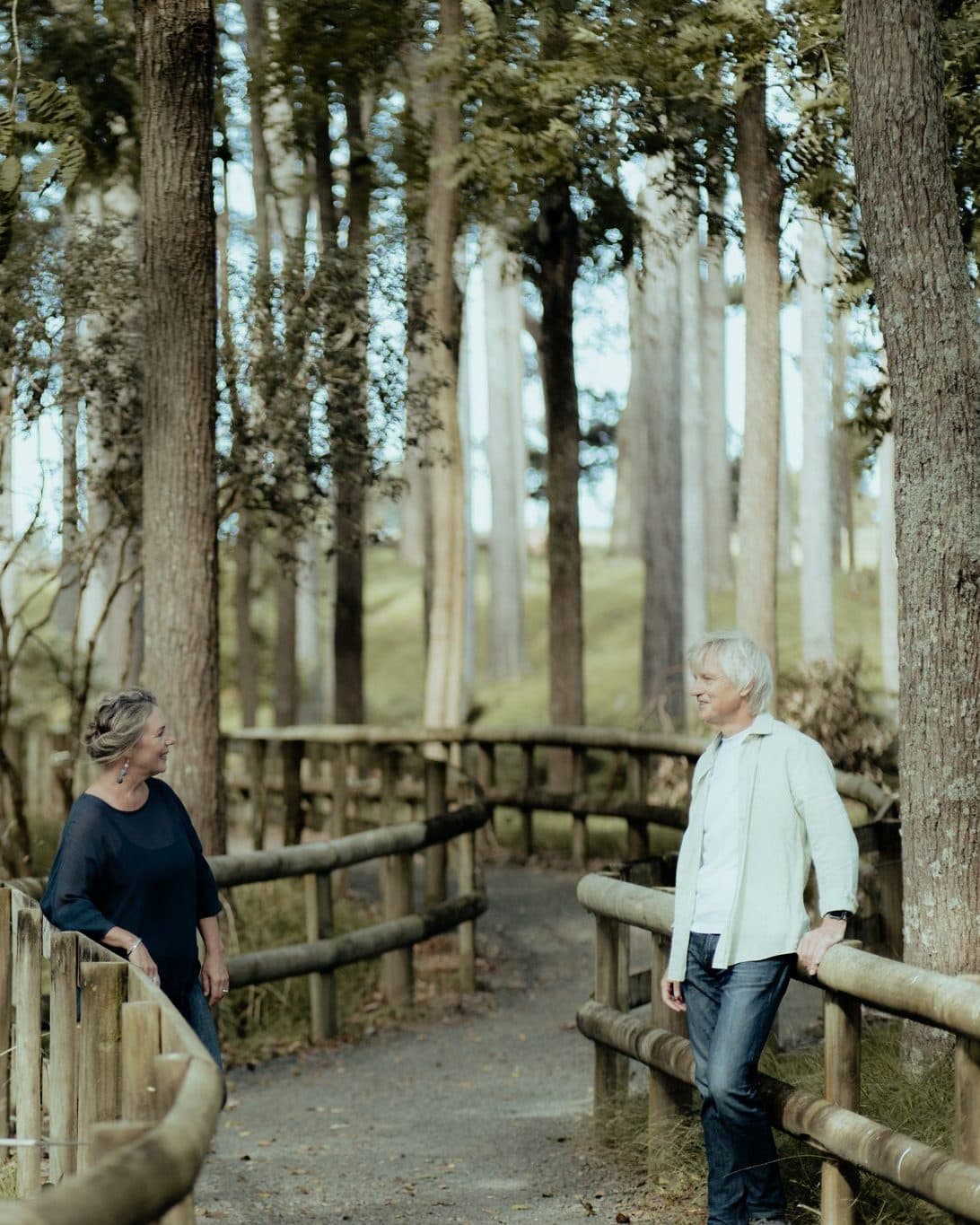 Mike and Lisa talking across a wooden bridge rail under tall trees